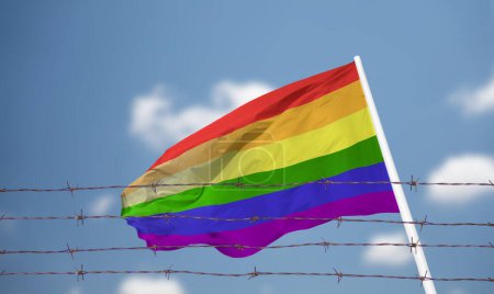 Photo for LGBTQ flag waving in the breeze inside a prison with a barbed wire fence and a blue sky with clouds. - Royalty Free Image