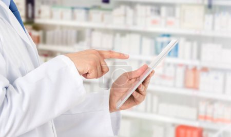 Téléchargez les photos : Tournage d'un pharmacien méconnaissable prenant des notes sur une tablette numérique dans une pharmacie - en image libre de droit