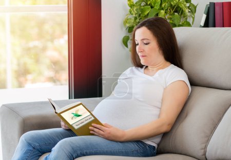 Foto de Un disparo de una joven embarazada leyendo un libro de bebés en casa. Todos los gráficos de pantalla se componen por nosotros - Imagen libre de derechos