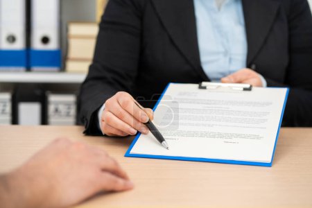 Photo for Close up of an executive hands holding a pen and indicating where to sign a contract at office - Royalty Free Image