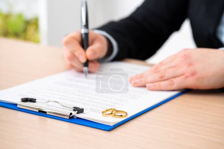 Foto de Primer plano del documento de divorcio de la firma de la esposa con anillos de boda sobre él en casa - Imagen libre de derechos