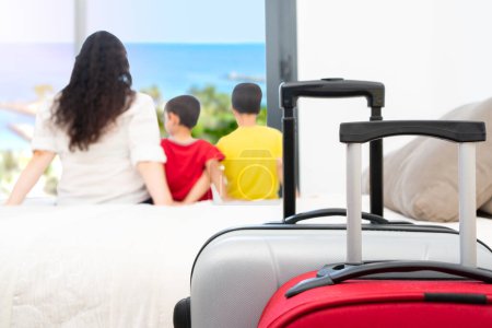 Rückansicht einer Touristenfamilie einer Mutter mit Kindern, die nach ihrer Ankunft mit Koffern im Vordergrund entspannt aus einem Hotelzimmerfenster blickt