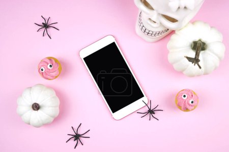 Photo for Pink Halloween smartphone evite ecard greeting card, party invitation mockup. Trick or treat party styled with white skull, pumpkins, black spiders, and spooky cupcakes. Negative copy space. - Royalty Free Image