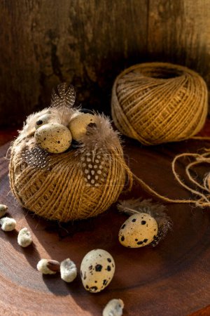 Téléchargez les photos : Œufs de caille, plumes de caille sur un écheveau de fil sur un fond de bois foncé - en image libre de droit