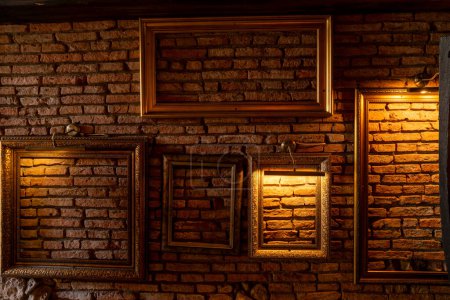 Photo for Vintage picture frames hanging on a red brick wall and illuminated by lamps - Royalty Free Image