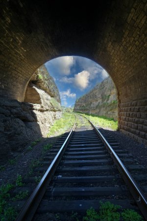 Téléchargez les photos : Depuis le tunnel ferroviaire, une vue du bout du tunnel et des rails allant dans la distance entre deux rochers contre le ciel - en image libre de droit
