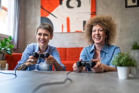 Téléchargez les photos : Deux femmes caucasiennes amies ou sœurs jouant à des jeux vidéo sur la console à la maison tenant manettes de jeu ayant plaisir femmes mûres heureuses personnes réelles copier l'espace - en image libre de droit