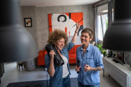 Téléchargez les photos : Deux femmes adultes matures amis caucasiens ou sœurs s'amusant à la maison femmes dansant et chantant karaoké tenir microphone écouter la musique heureux sourire rythme joyeux vraies personnes copier l'espace - en image libre de droit