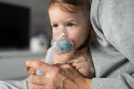 Photo for One toddler using nebulizer at home small girl child using vapor steam inhaler mask inhalation at home medical procedure medicament treatment asthma pneumonia bronchitis selective focus - Royalty Free Image
