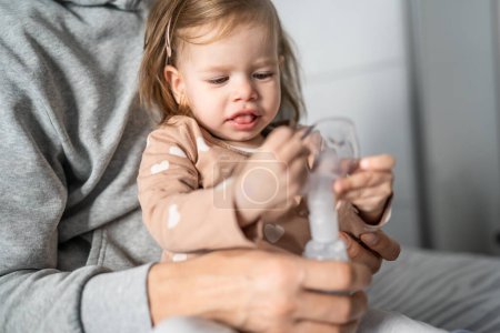 Photo for One toddler using nebulizer at home small girl child using vapor steam inhaler mask inhalation at home medical procedure medicament treatment asthma pneumonia bronchitis selective focus - Royalty Free Image