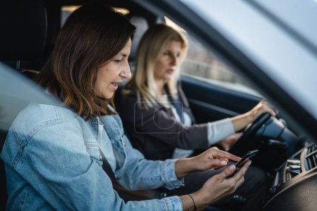 Zwei Frauen fahren im Auto reife kaukasische Freundinnen überprüfen Handy Urlaubskonzept Online-Karte Planung der Reiseroute im Auto in Tag echte Menschen kopieren Raum Smartphone-App und GPS