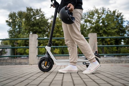 Foto de Pies de hombre desconocido de pie o conducción eléctrica patinete scooter e-scooter en el pavimento en el transporte moderno ecológico día - Imagen libre de derechos