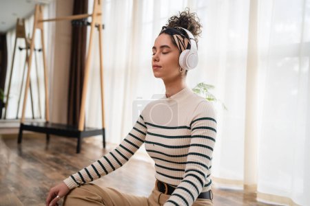eine erwachsene kaukasische Millennial mit Kopfhörern für Online-geführte Meditation praktiziert Achtsamkeit Yoga mit geschlossenen Augen auf dem Boden zu Hause echte Menschen Selbstpflege-Konzept kopieren Raum