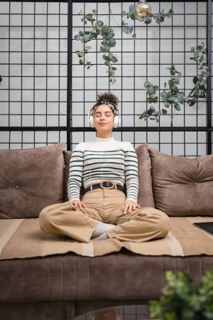 Téléchargez les photos : One woman adult caucasian female millennial using headphones for online guided meditation practicing mindfulness yoga with eyes closed on the sofa bed at home real people self care concept copy space - en image libre de droit