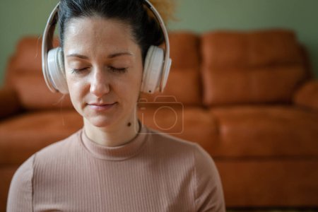 una mujer adulta caucásica milenaria usando auriculares para meditación guiada en línea practicando mindfulness yoga con los ojos cerrados en el suelo en casa personas reales autocuidado concepto de espacio de copia