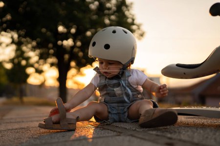 Photo for One girl small caucasian toddler child fall of the children's kick scooter wear protective helmet while playing outdoor in summer evening real people leisure growing up concept copy space - Royalty Free Image