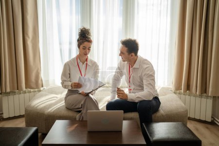 Téléchargez les photos : Two people man and woman colleagues sitting together at hotel room with contracts and documents preparing for sales meeting or conference making plans sharing experience real people business concept - en image libre de droit