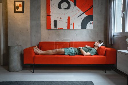 Foto de One man adult caucasian male on bed sofa use headphones for online guided meditation practicing mindfulness yoga with eyes closed at home real people self care manifestation concept copy space - Imagen libre de derechos
