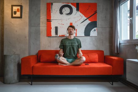 ein Mann erwachsenen kaukasischen Mann verwenden Kopfhörer für Online-geführte Meditation praktizieren Achtsamkeit Yoga mit geschlossenen Augen zu Hause echte Menschen Selbstpflege Manifestationskonzept kopieren Raum