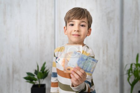 Téléchargez les photos : Portrait d'un garçon caucasien de six ans détenant des billets en euros épargne - en image libre de droit