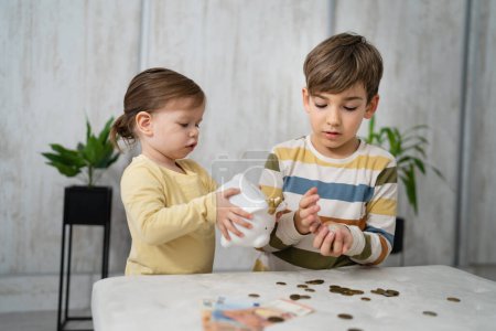Téléchargez les photos : Siblings boy and girl small caucasian child brother and sister play at home with piggy bank saving money childhood investment insurance and finance concept copy space - en image libre de droit