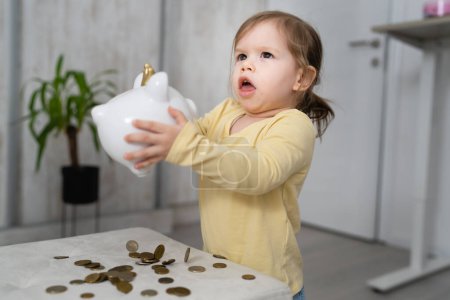 Photo for One small caucasian girl two years old play with coins and piggy bank at home insurance money saving and future investment concept - Royalty Free Image