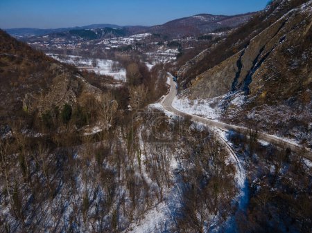 Téléchargez les photos : Vue aérienne sur drone sur la route à travers la colline et la montagne en journée d'hiver couverte de neige avec des roches et des arbres - en image libre de droit