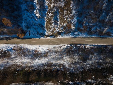 Téléchargez les photos : Vue aérienne sur drone sur la route à travers la colline et la montagne en journée d'hiver couverte de neige avec des roches et des arbres - en image libre de droit
