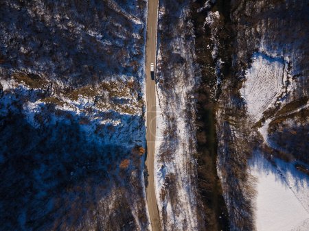 Foto de Vista aérea del dron en el camino a través de la colina y la montaña en el día de invierno cubierto de nieve con roca y árboles y río - Imagen libre de derechos