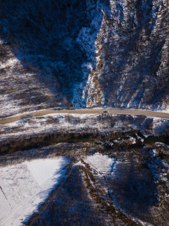 Téléchargez les photos : Aerial drone view on the road trough the hill and mountain in winter day covered with snow with rock and trees and river - en image libre de droit