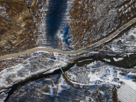 Photo for Aerial drone view on the road trough the hill and mountain in winter day covered with snow with rock and trees and river - Royalty Free Image