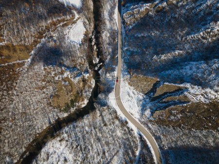Foto de Vista aérea del dron en el camino a través de la colina y la montaña en el día de invierno cubierto de nieve con roca y árboles y río en Serbia - Imagen libre de derechos