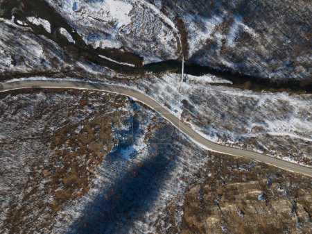 Téléchargez les photos : Vue aérienne sur drone sur la route à travers la colline et la montagne en journée d'hiver couverte de neige avec des rochers et des arbres et rivière en Serbie - en image libre de droit