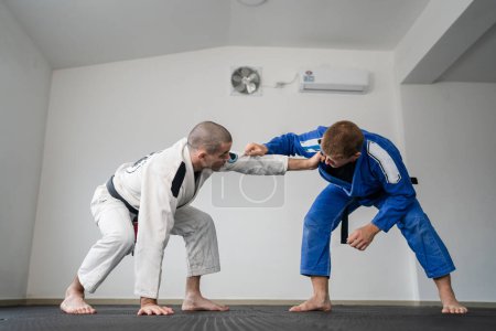 Téléchargez les photos : Brésilien jiu jitsu bjj entraînement ou épargner deux athlètes combattants aneth technique des arts martiaux à la salle de gym sur les tapis tatami porter kimono gi ceinture noire instructeur démontrer la technique debout - en image libre de droit