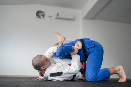 Photo for Brazilian jiu jitsu bjj training or sparing two athletes fighters dill martial arts technique at gym on the tatami mats wear kimono gi black belt instructor demonstrate submission kimura - Royalty Free Image