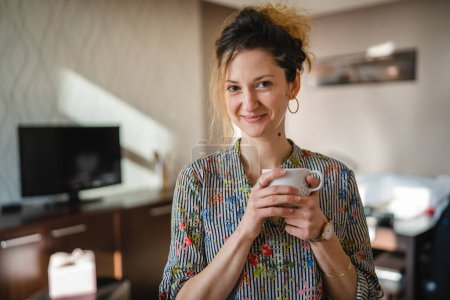 Photo for One woman happy caucasian female standing at home or hotel apartment with cup of coffee daily morning routine taking a brake real people copy space - Royalty Free Image