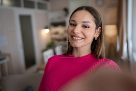 Foto de Front view portrait of one caucasian woman young female stand in her apartment at home wear sweater happy confident real people copy space UGC selfie user generated content happy smile - Imagen libre de derechos