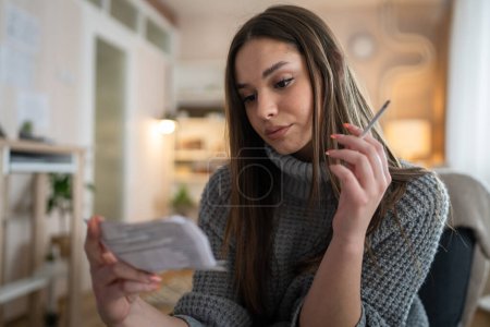 Foto de Una mujer joven caucásica hembra sentarse en casa humo cigarrillo leer nota - Imagen libre de derechos