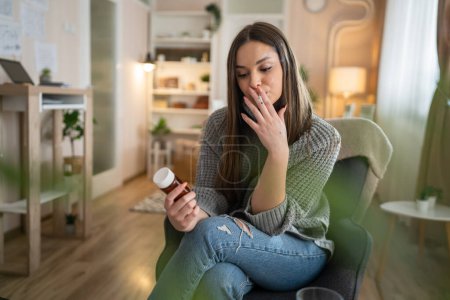 Foto de Una mujer joven caucásica hembra mantenga medicamentos pastillas tabletas mientras está sentado en casa fumar cigarrillo pensando en tratar de dejar de fumar espacio de copia persona real - Imagen libre de derechos