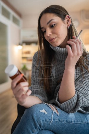 Photo for One woman young caucasian female hold medicine drugs pills tablets while siting at home smoke cigarette thinking trying to quit smoking real person copy space - Royalty Free Image