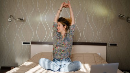 Foto de One woman adult caucasian female sit on the bed in hotel room or at home doing yoga exercise stretching daily morning routine copy space - Imagen libre de derechos