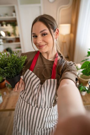 Foto de One woman young caucasian female stand at home hold flower plants pot happy smile self portrait UGC User Generated Content front view gardening and botany horticulture care concept copy space - Imagen libre de derechos