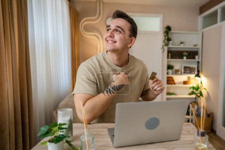Photo for One man adult caucasian male sit at home happy smile at laptop computer hold bank credit card online shopping concept real people copy space e-commerce - Royalty Free Image