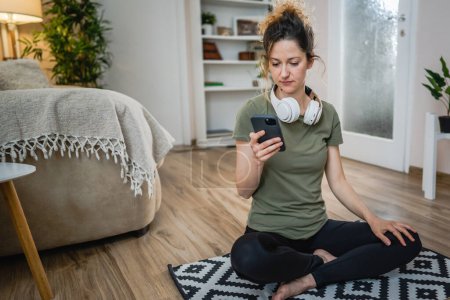 Foto de One woman sit on the floor at home with headphones use smart-phone for music listening or search for podcast online meditation or audiobook on her smarphone mobile phone online on internet copy space - Imagen libre de derechos