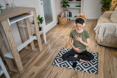 una mujer adulta caucásica milenaria usando auriculares para la meditación guiada en línea practicando mindfulness yoga con los ojos cerrados sentarse en el suelo en casa personas reales autocuidado concepto copia espacio