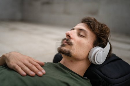 Photo for One man young adult caucasian male eyes closed for guided training yoga or meditation while sitting outdoor with headphones self-care practice real people well-being inner peace and balance concept - Royalty Free Image