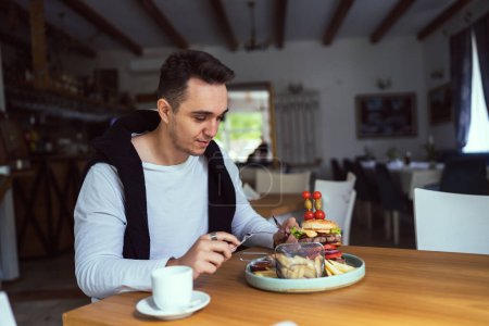 Téléchargez les photos : Un homme jeune homme caucasien adulte assis à la table au restaurant avec des burghers et des frites de pommes de terre feu français manger seul dans la journée personnes réelles copier l'espace - en image libre de droit