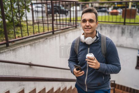 Photo for One man young adult male walking up the stairs steps in the city in day with cup of coffee and mobile phone real people tourist or student copy space - Royalty Free Image