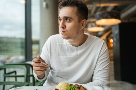 Téléchargez les photos : Un homme jeune homme caucasien adulte assis à la table dans un restaurant public manger des personnes réelles copier l'espace - en image libre de droit