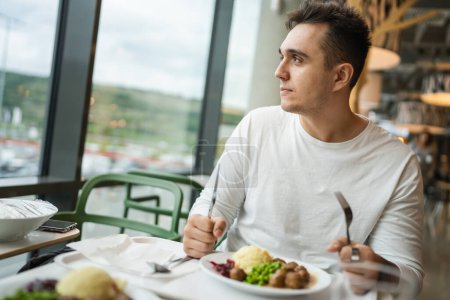 Téléchargez les photos : Un homme jeune homme caucasien adulte assis à la table dans un restaurant public manger des personnes réelles copier l'espace - en image libre de droit